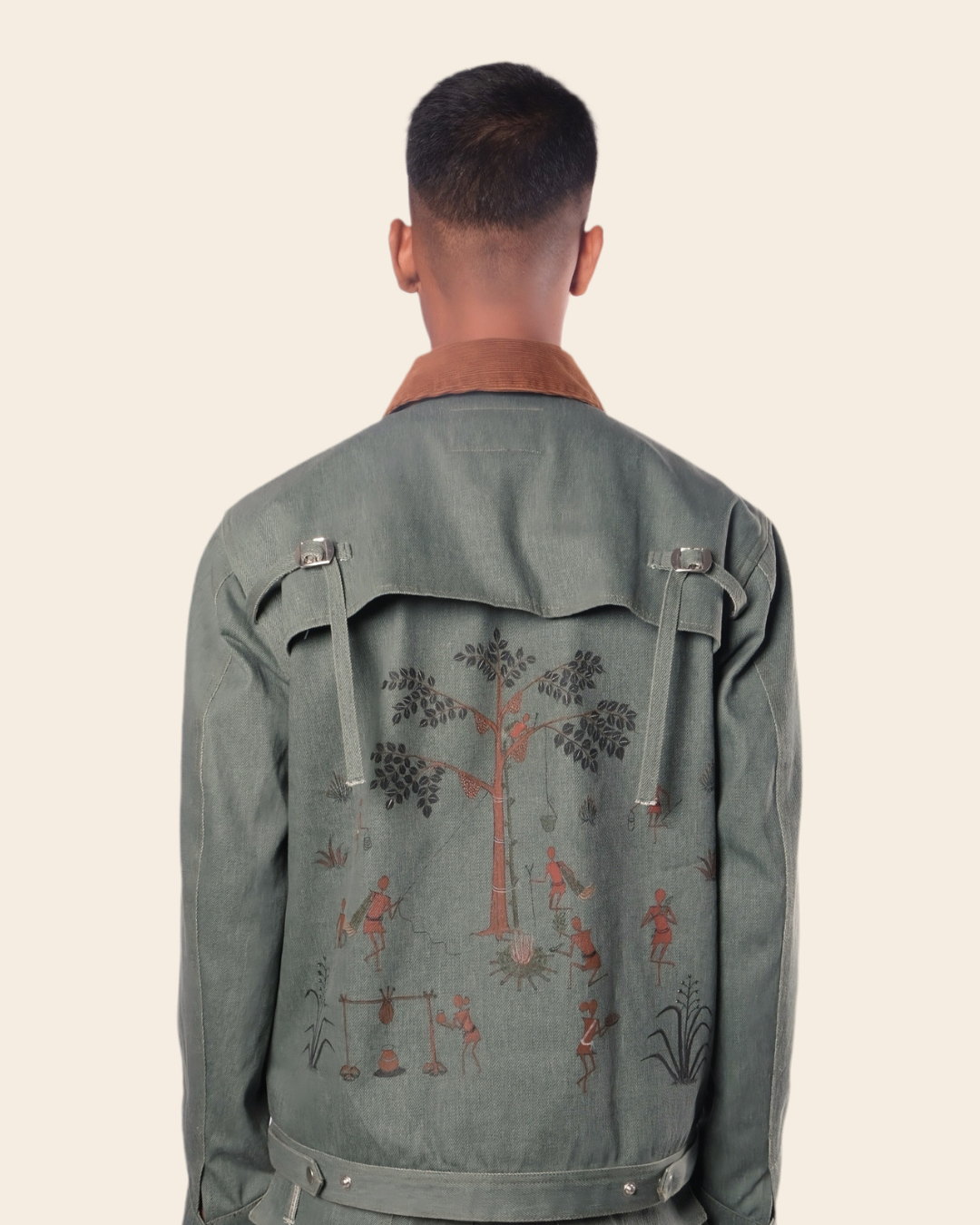 Person wearing a green jacket with embroidered designs on the back against a beige background