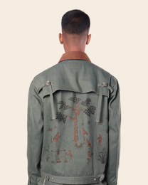 Person wearing a green jacket with embroidered designs on the back against a beige background