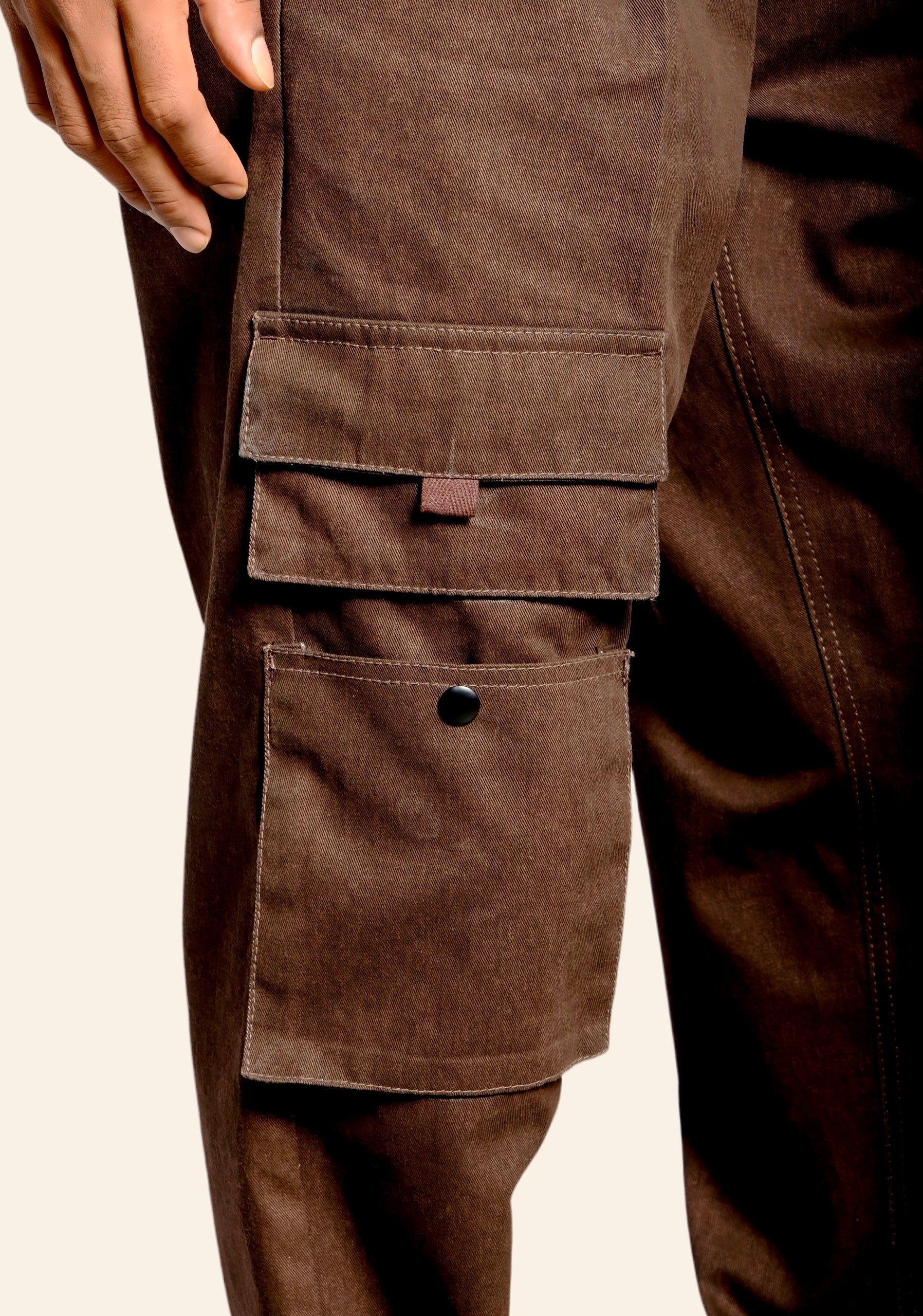 Close-up of brown cargo pants with multiple pockets on a beige background